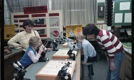 Open House 1986; children using microscopes with adults watching [photograph 1 of 2]