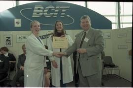 Open House 1998; student in lab coat shakes hands with man while student in lab coat behind them ...