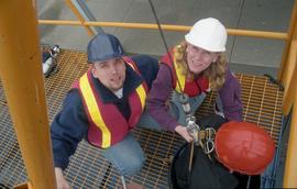 Open House 1998; two people in safety vests looking up to camera while third sitting in a pulley ...