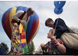 Open house 1992; clown on stilts waving at mother and child in front of hot air balloon [photogra...