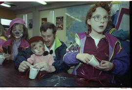 Open house 1992; father helping with craft while children stare into camera