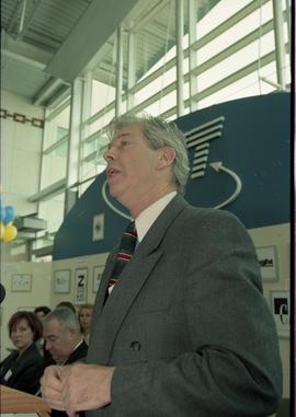 Open House 1998; older man wearing stripped tie speaks on stage behind podium