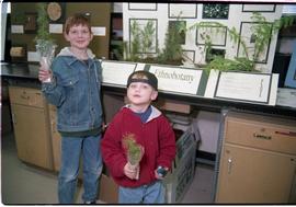 Open House 1998; two boys holding up plants in front of ethnobotany display [photograph 2 of 2]