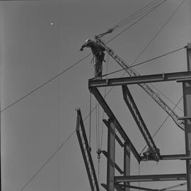 Structural steel, 1971; worker standing at the top of a steel structure; steel beam being moved u...