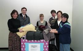 Staff members with a box labeled "Warm clothes and blankets for the needy" [2 of 5 phot...