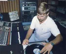 Broadcast Communications; man using a record player in a radio control booth