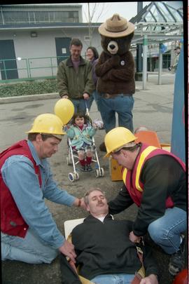Open House 1998; two men demonstrating placing another man on first aid board while Smokey the Be...