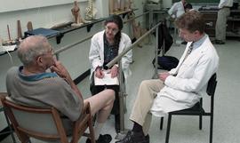 Two people in lab coats talking to an amputee [2 of 2 photographs]