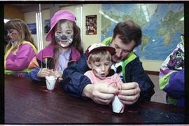 Open house 1992; father helping child with craft while other child smiles to camera