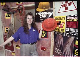 Open House 1992; woman posing with hard hat in front of safety signs [photograph 2 of 3]
