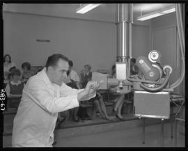 Medical radiography, 1967; man in a lab coat using radiography apparatus ; people sitting at desk...