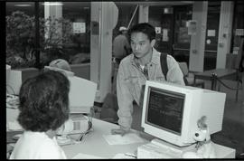 Communications Relations Opening Day 1991; man listening while registrar worker sits in front of ...