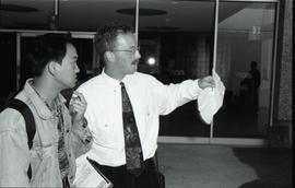 Communications Relations Opening Day 1991; man in tie holding paper  beside student in jean jacke...