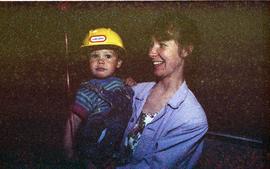 Open house 1992; woman holding toddler wearing toy hard hat