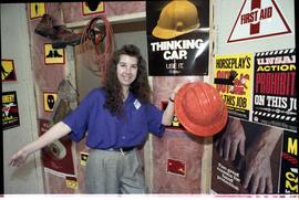 Open House 1992; woman posing with hard hat in front of safety signs [photograph 2 of 3]