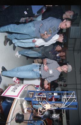 Open House 1998; man presenting machine display in front of various people in display hall
