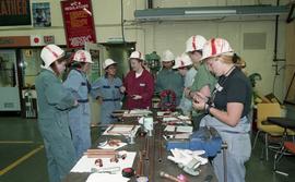 Trades discovery for women; piping, students in helmets and uniforms standing around a table with...