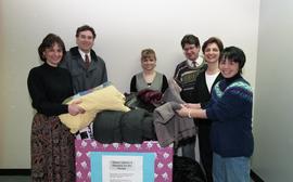 Staff members with a box labeled "Warm clothes and blankets for the needy" [1 of 5 phot...