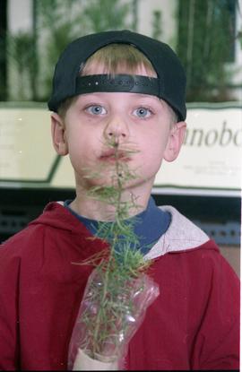 Open House 1998; child in baseball cap holding plant in front of face