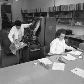 BCVS Graphic arts ; woman using a paper collator ; woman organizing papers at a desk