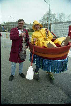 Open House 1998; man dressed in raincoat and row boat with man holding dead plastic fish [photogr...