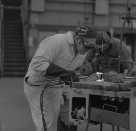 Welding, 1968; man wearing protective goggles and gloves welding ; man working in background [2 o...