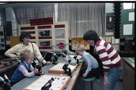 Open House 1986; children using microscopes with adults watching [photograph 2 of 2]