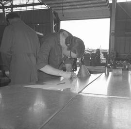 Sheet metal, 1968; student cutting a piece of sheet metal ; people working in background