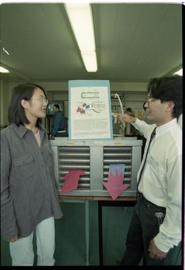 Open House 1998; student in business attire explains heat pipe to woman [photograph 1 of 2 ]