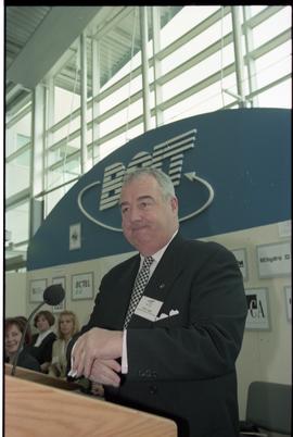 Open House 1998; Peter Legge stands with hands folded in mid air on Open House BCIT stage