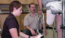 Two people with person supported by walker and special apparatus