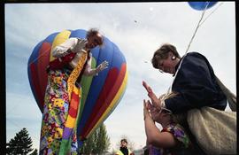 Open house 1992; clown on stilts waving at mother and child in front of hot air balloon [photogra...
